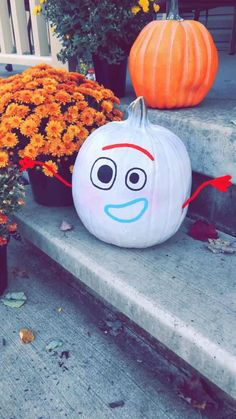 two pumpkins with faces painted on them sitting on the steps next to some flowers