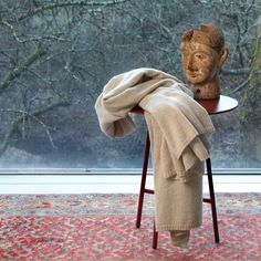 a chair with a blanket on top of it next to a statue in front of a window