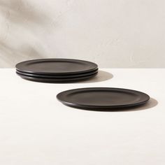 two black plates sitting next to each other on a white tableclothed surface with a wall in the background