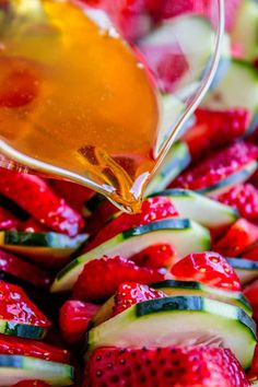 someone is pouring honey over sliced cucumbers and strawberries to make fruit salad