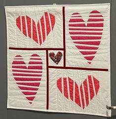 four red and white heart quilts hanging on a wall