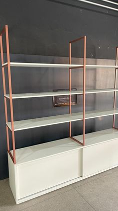 three white shelves with copper metal brackets on each shelf and a sign in the middle