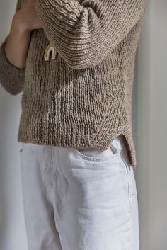 a woman in white pants and a brown sweater is holding her hands on her hips