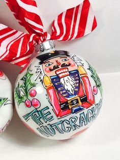 two christmas ornaments with red and white striped ribbons on the top one has an ornament that says the nutcracker