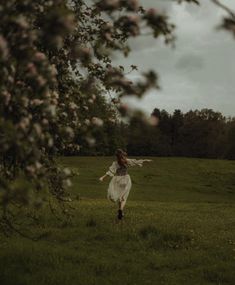 a woman in a white dress is walking through the grass with her arms spread out