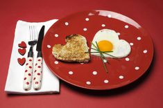 a heart - shaped fried egg and toast on a red plate with white polka dots