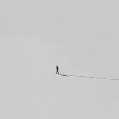 a man walking across a snow covered field with a kite in the sky behind him