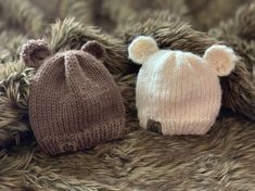 two knitted hats laying next to each other on top of a fur covered surface