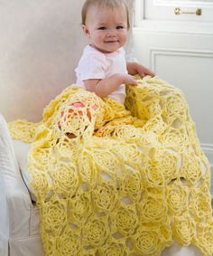 a baby is sitting on a chair with a yellow crocheted blanket over it