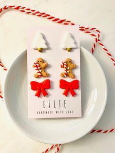 a pair of gingerbread man earrings with red bows and candy canes on a white plate