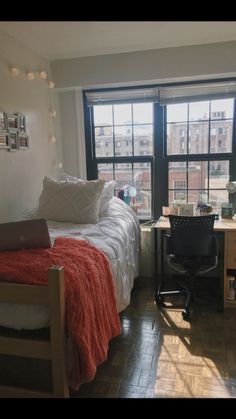 a bed room with a neatly made bed and a laptop on a desk in front of a window