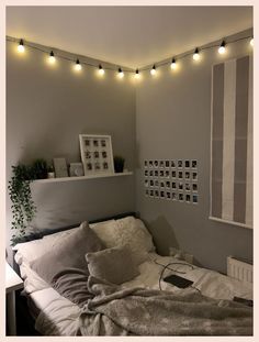 an unmade bed in a small room with string lights on the wall above it