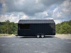 a black trailer parked in a parking lot next to some rocks and trees on a cloudy day