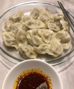 a bowl of sauce next to a plate of dumplings