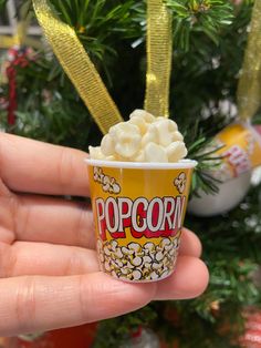 a hand holding up a small cup filled with popcorn next to a christmas ornament