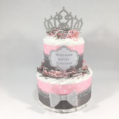 a three tiered cake with pink and gray decorations on top, topped with a tiara