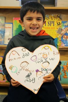 a young boy holding up a heart shaped sign in front of a book shelf filled with children's books