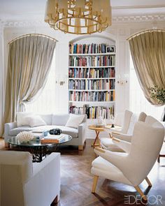 a living room filled with white furniture and a book shelf full of books on top of it