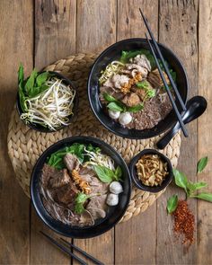 three black bowls filled with food on top of a wooden table next to chopsticks