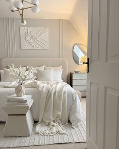 a white bed with pillows and blankets on top of it next to a mirror in a room