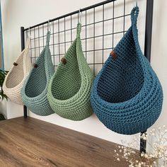 three crocheted baskets hanging on a wall in front of a potted plant