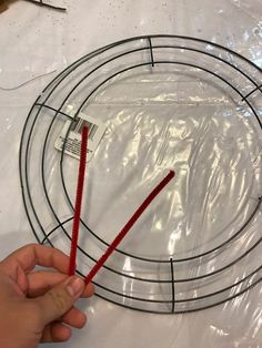 a person is holding two red wires in front of a circular wire rack on a table