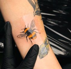 a bee tattoo on someone's arm with black gloves and a rubber glove next to it