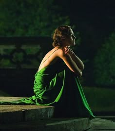 a woman in a green dress is sitting on the steps and looking off into the distance