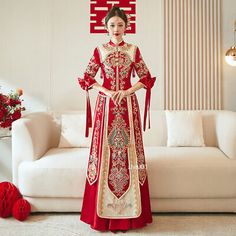 a woman standing in front of a white couch wearing a red and gold chinese dress