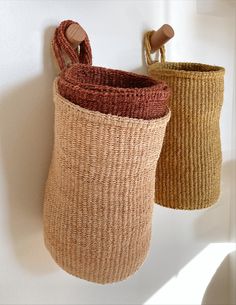 two woven baskets hang on the wall next to each other, one has a wooden handle