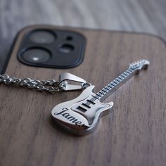 a guitar keychain sitting on top of a wooden table next to an iphone