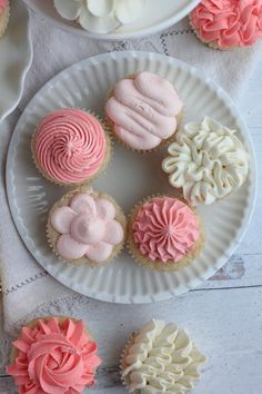 some cupcakes are on a white plate with pink and white frosted icing