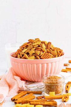 a pink bowl filled with cheetos next to a glass of milk and some pretzels