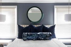 a bedroom with blue walls, white bedding and large round mirror on the wall