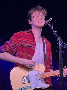 a young man is playing an electric guitar and singing into a microphone at a concert