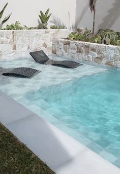 an empty swimming pool with lounge chairs in the grass next to it and a stone wall behind it