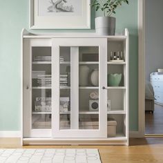 a grey bookcase with glass doors and shelves in the corner next to a white rug