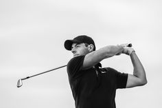 a black and white photo of a man swinging a golf club at a ball on the tee