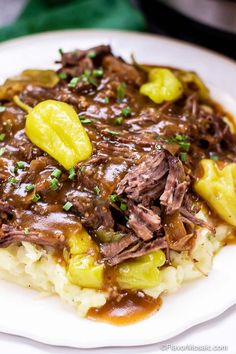 a white plate topped with meat and potatoes covered in gravy on top of mashed potatoes