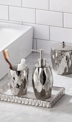 three pieces of bathroom accessories on a marble countertop in a white tiled bathroom area