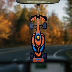 an orange and blue toy car hanging from the side of a car window with trees in the background