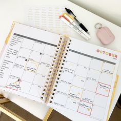 an open planner sitting on top of a desk next to a pen and marker holder