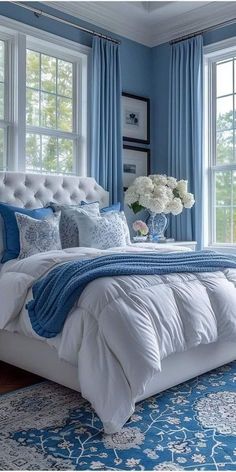 a bedroom with blue walls and white bedding, windows, and rugs on the floor