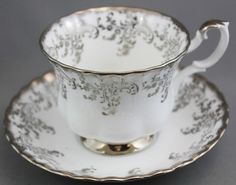 an antique tea cup and saucer with silver trimmings on the rim, set against a gray background