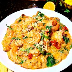 pasta with shrimp, spinach and cheese on a white plate next to lemon wedges