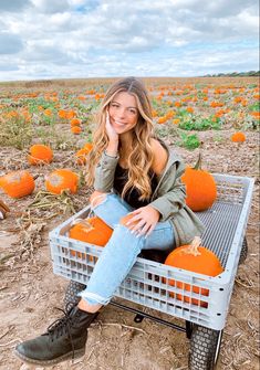 a woman sitting on a crate in a pumpkin field