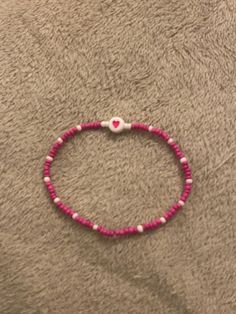 a pink beaded bracelet with white beads and a heart on the end is laying on a gray surface