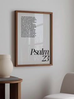 a white vase sitting on top of a wooden table next to a framed poster above it