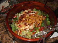 a salad in a bowl on top of a counter next to a knife and fork