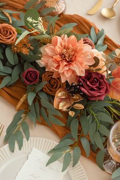 an arrangement of flowers and greenery on a place setting for a formal dinner table